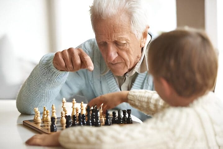 Elderly man playing chess with a young child.